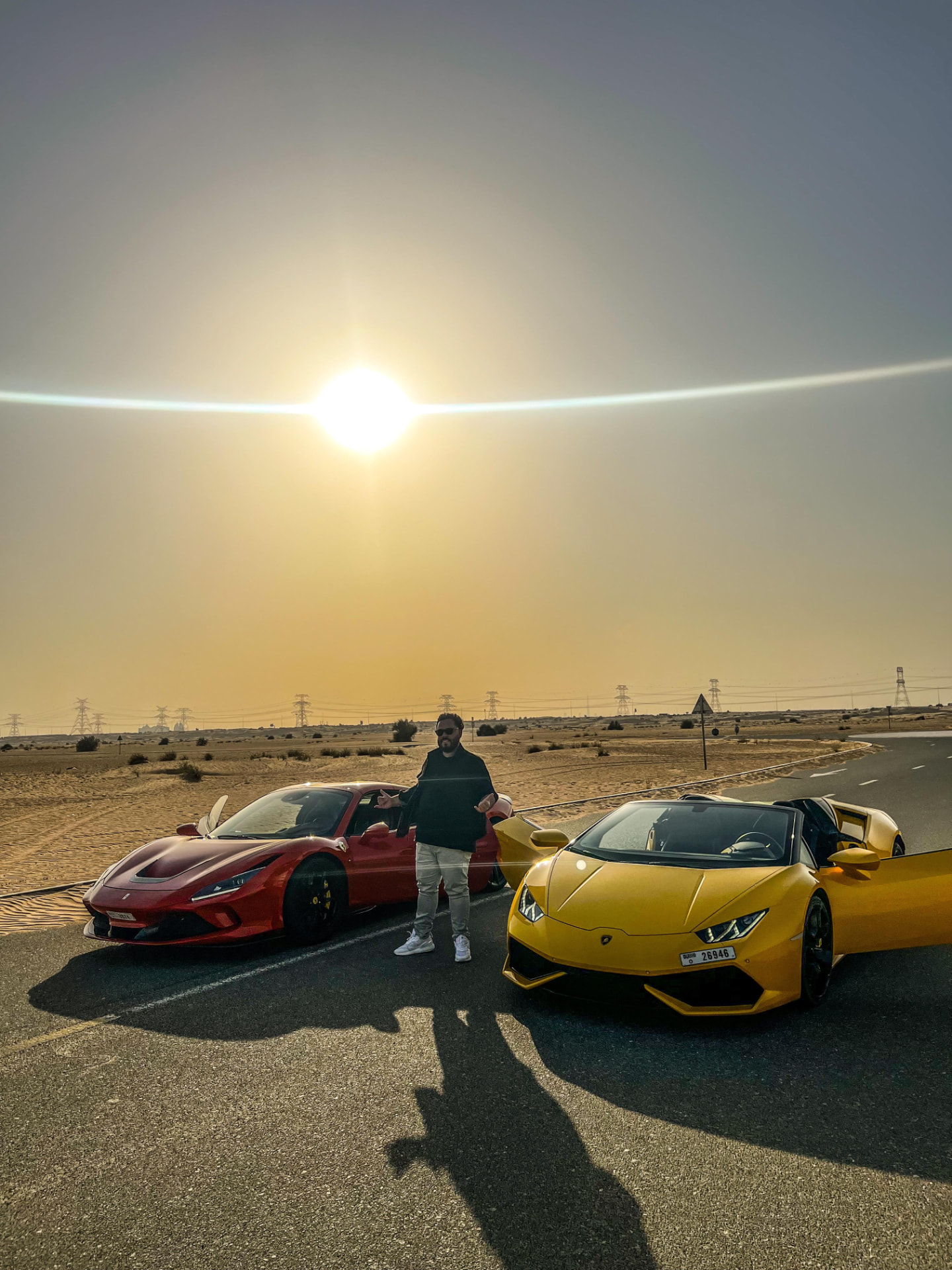 Ferrari vermelha e Lamborghini amarela em estrada no deserto ao pôr do sol